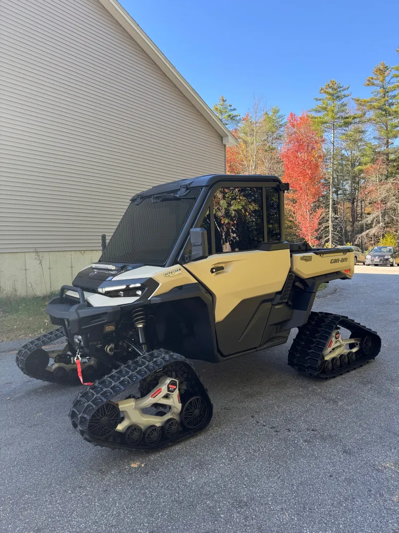 Tan Can-Am Defender on tracks outside the shop with tinted cab glass for winter glare.