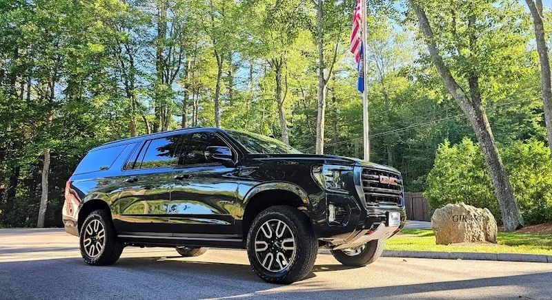 Black GMC Yukon XL with tinted side glass parked on a tree-lined New Hampshire drive.