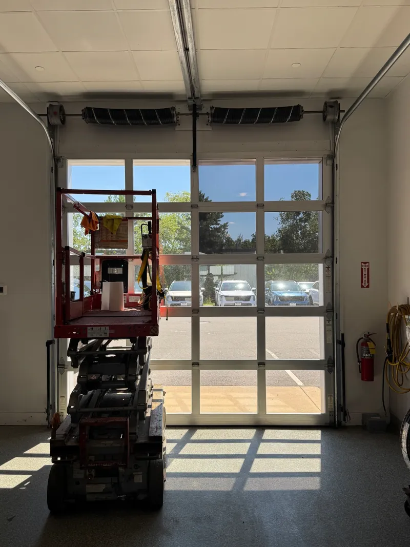 Interior view of a filmed glass overhead door cutting afternoon glare inside a service bay.