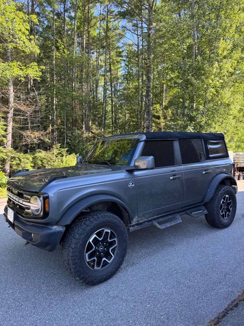Gray four-door Ford Bronco with a soft top and freshly tinted side and rear glass.