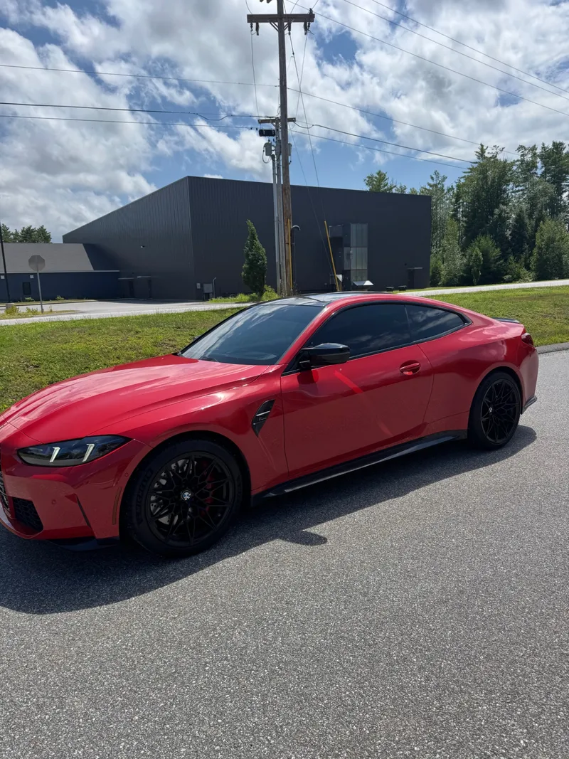 Red BMW M4 Competition parked outside the shop with dark tint on every side window.